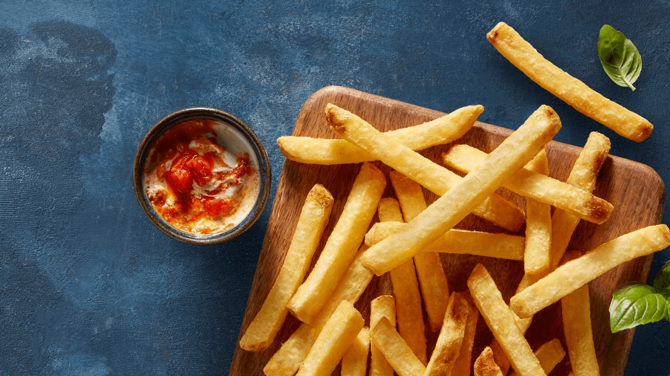 Bästa pommes frites Aviko Sverige på en träbricka med röd sås och gröna blad, på en blå bakgrund.