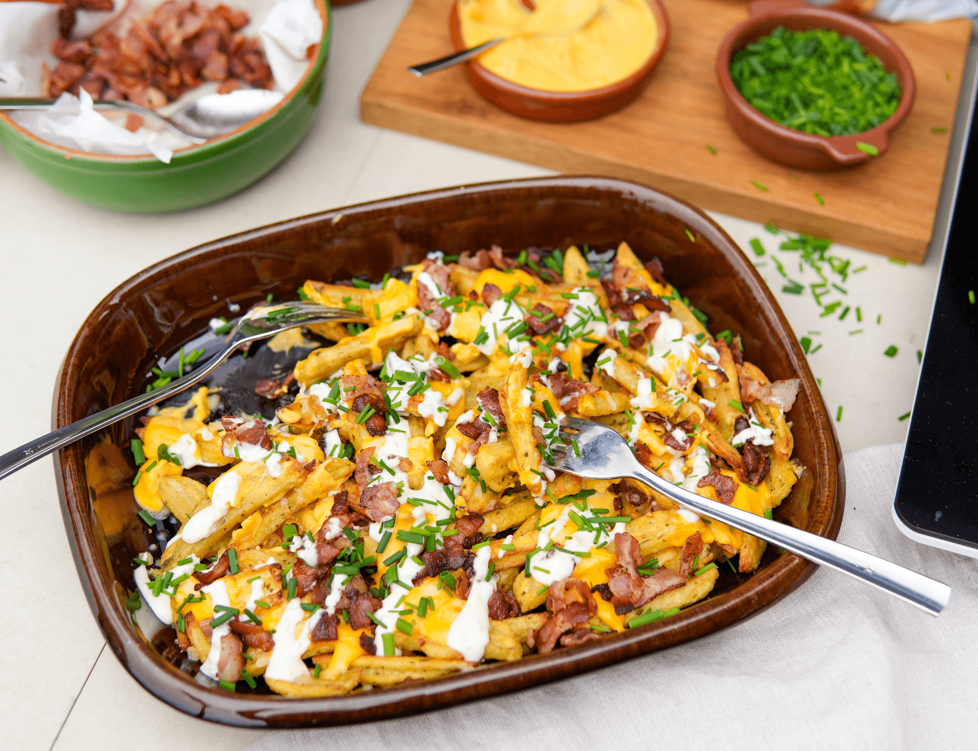 recept på loaded fries me knaprig bacon och vitlökssås. Avikos wavy blends som bas. Serverat i stor skål på en vit duk.